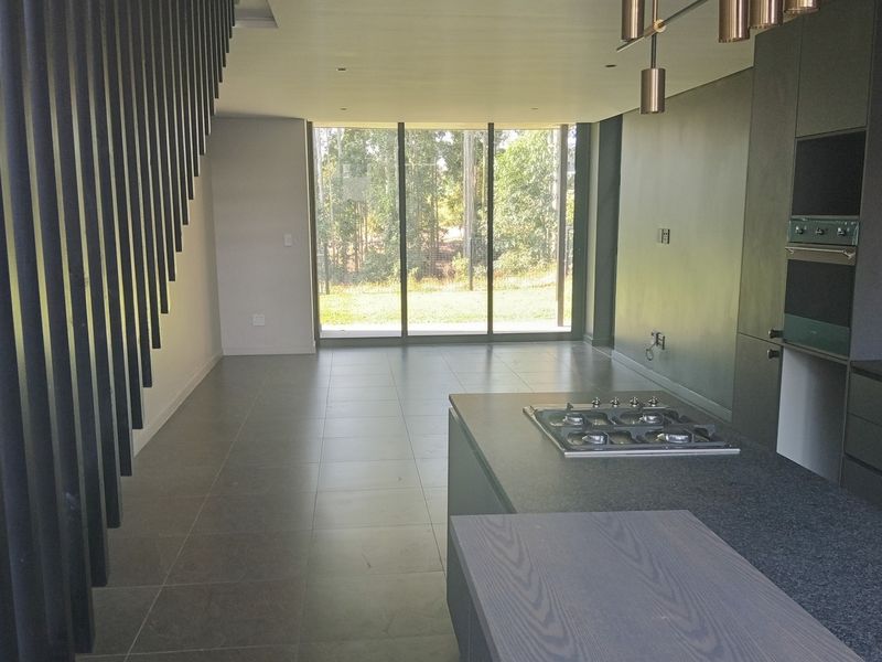 Modern open-plan living and kitchen area featuring sleek dark cabinetry, a stone island with gas cooktop, and large sliding doors leading to the garden.