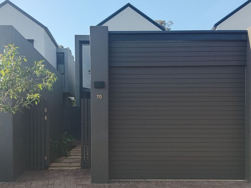 Modern townhouse exterior featuring a dark-toned garage door, timber slat fencing, and a paved driveway entrance.