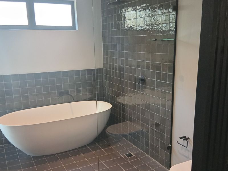 Modern bathroom featuring a sleek freestanding bathtub, a walk-in shower with glass screen, and contemporary dark tiled finishes.