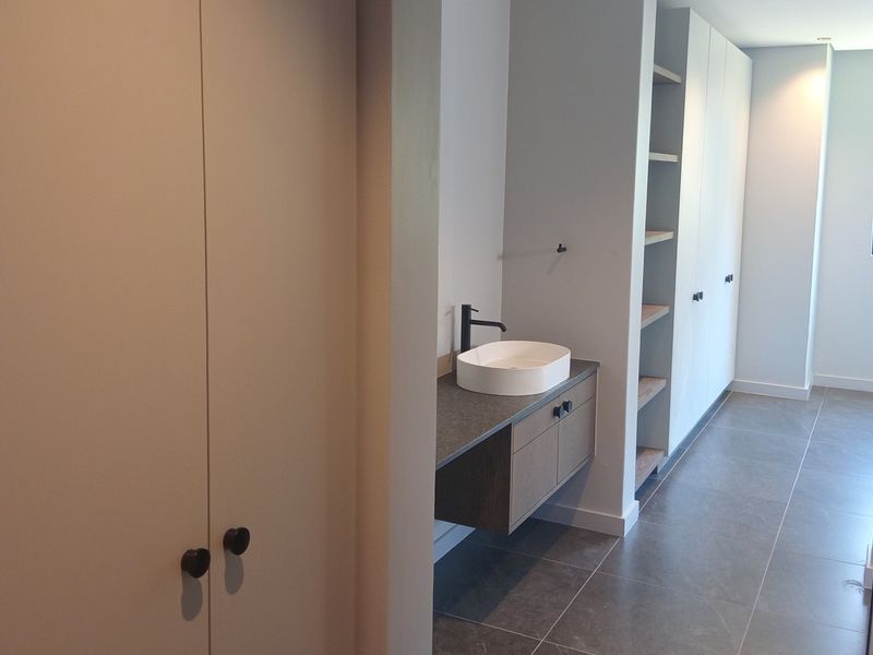 Modern bathroom featuring a floating vanity with a vessel sink, matte black fixtures, and extensive built-in storage cabinetry with clean, contemporary finishes.