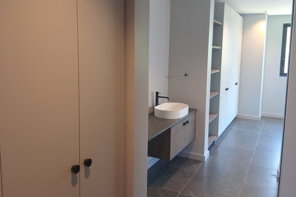 Modern bathroom featuring a floating vanity with a vessel sink, matte black fixtures, and extensive built-in storage cabinetry with clean, contemporary finishes.
