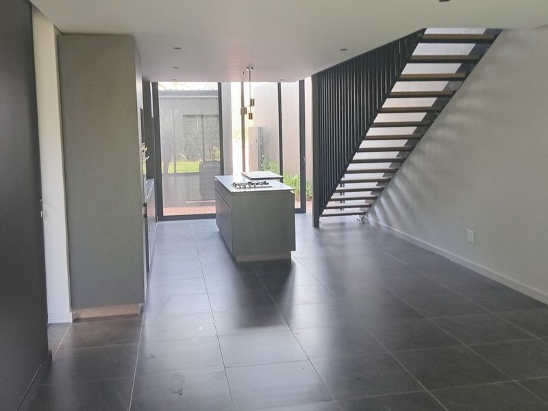 Modern open-plan living area featuring a sleek kitchen island with a built-in hob, contemporary staircase, and large sliding doors leading to the rear exterior.
