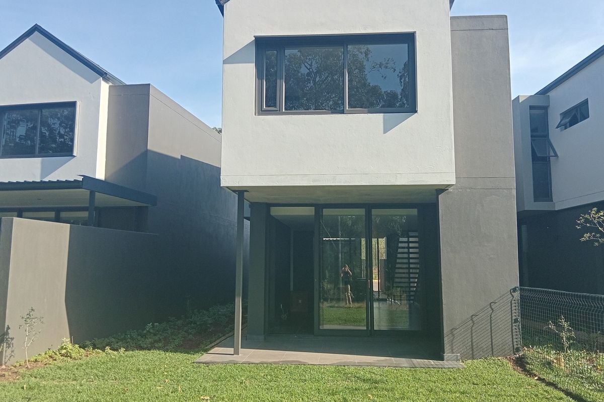 Rear view of a modern townhouse featuring a paved patio, sliding glass doors, and a private garden area.