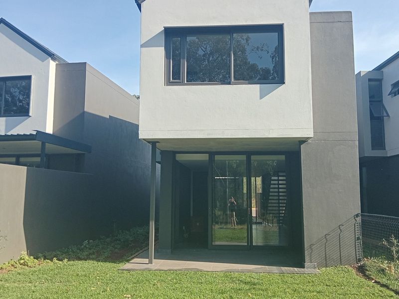 Rear view of a modern townhouse featuring a paved patio, sliding glass doors, and a private garden area.