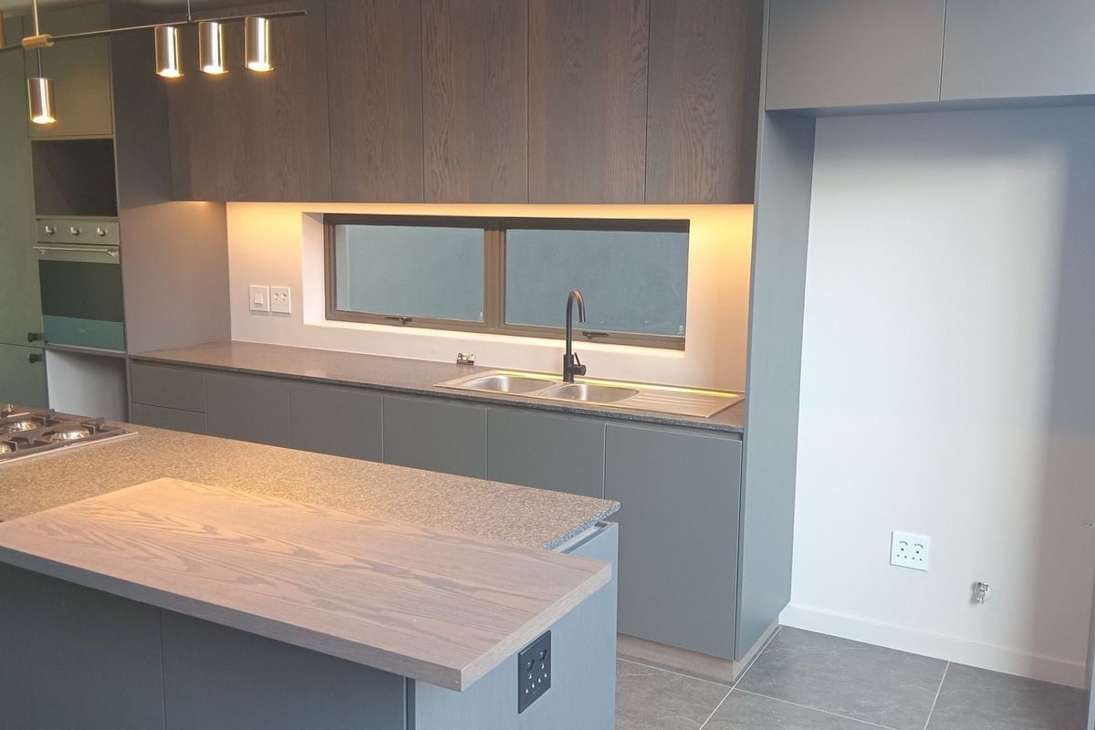 Modern kitchen featuring a central island, stone countertops, built-in oven, gas hob, and sleek cabinetry with integrated under-cabinet lighting.