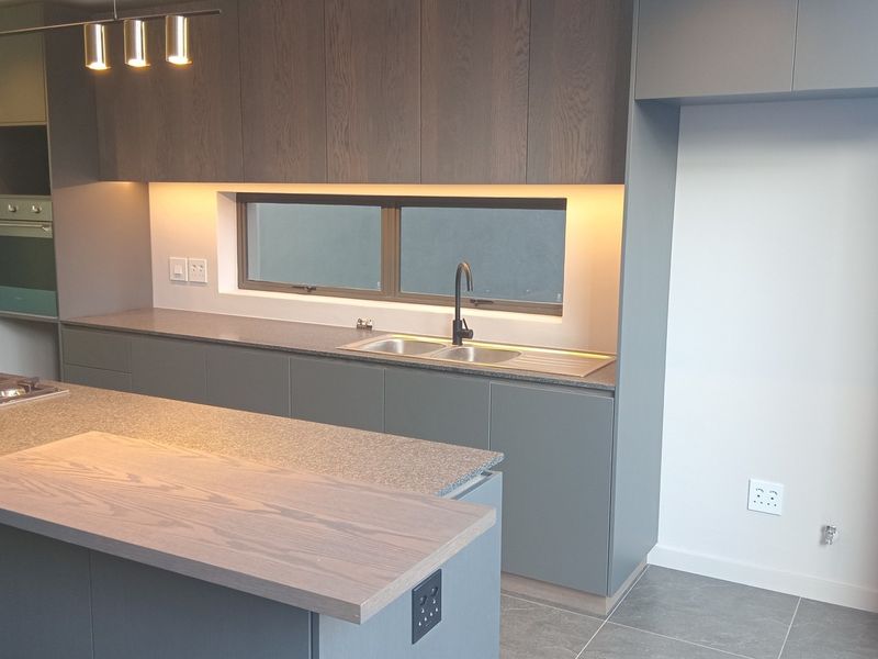 Modern kitchen featuring a central island, stone countertops, built-in oven, gas hob, and sleek cabinetry with integrated under-cabinet lighting.