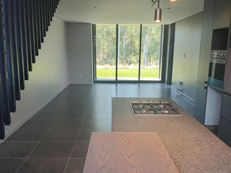Modern open-plan kitchen and living area featuring a central island with gas hob, built-in oven, sleek cabinetry, and large windows overlooking the garden.