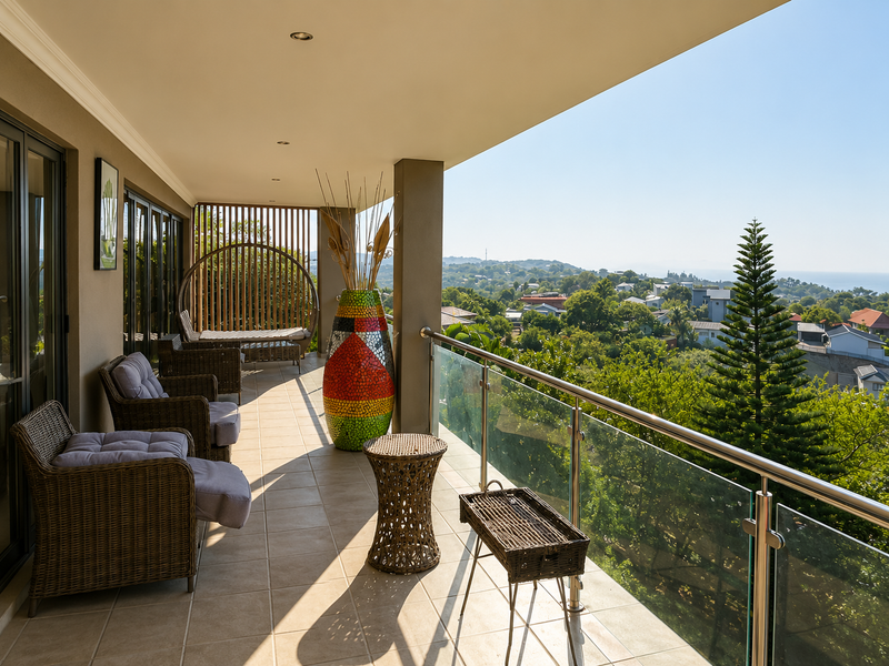 Spacious covered balcony featuring tiled flooring, a modern glass balustrade, and expansive elevated views over the surrounding neighbourhood.
