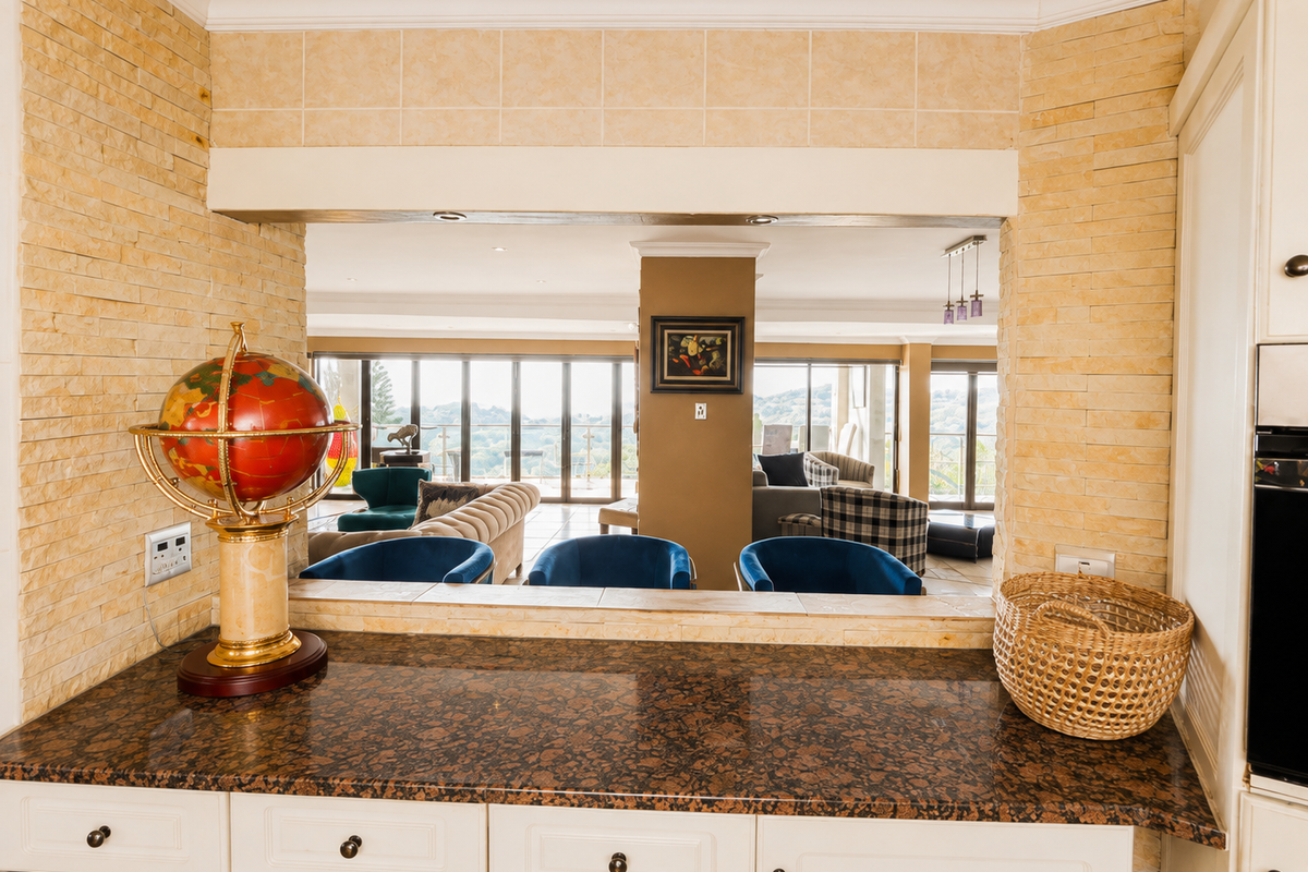 A kitchen pass-through window featuring granite countertops and stone veneer wall cladding, overlooking an open-plan living area with expansive views.