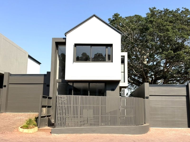 Modern townhouse exterior featuring a clean gabled facade, paved driveway, secure slatted fencing, and automated garage access.
