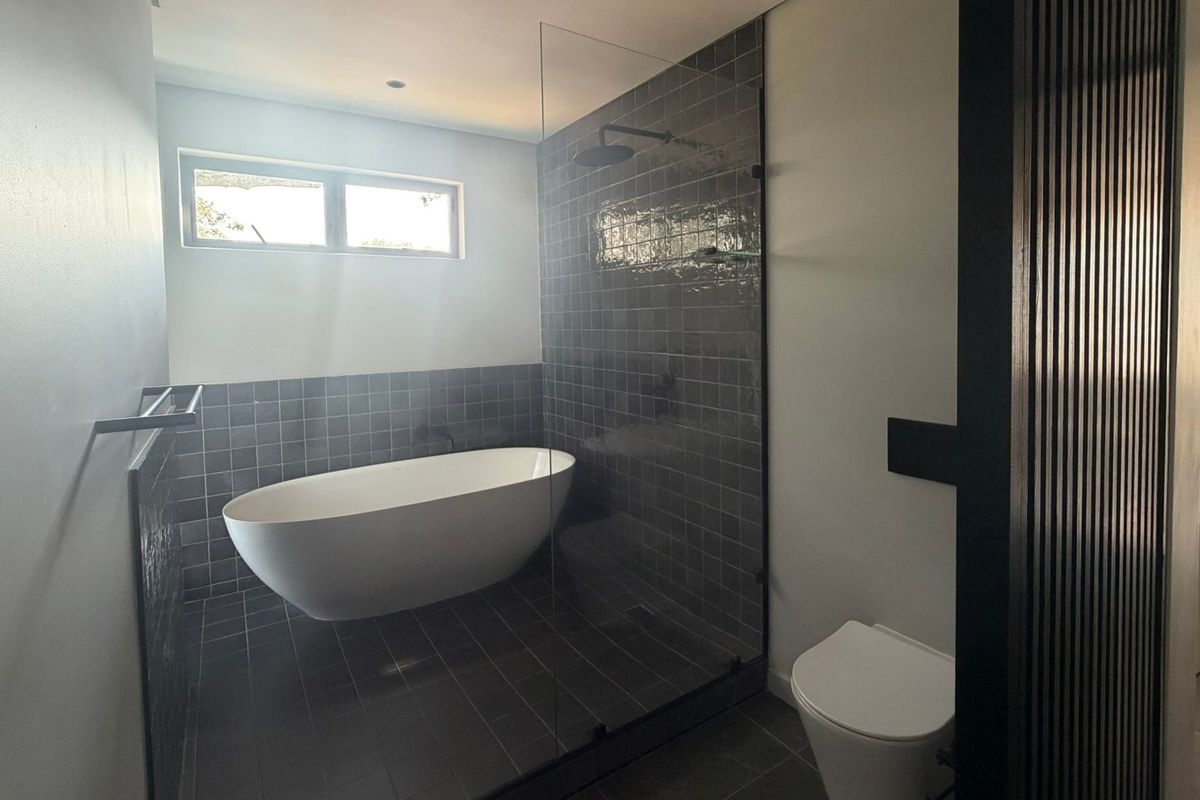 Modern bathroom featuring a sleek freestanding bathtub, a glass-enclosed shower with dark tiling, and a wall-hung toilet.