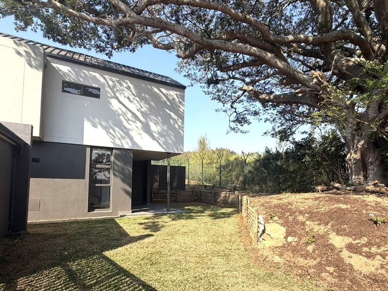 Rear view of the townhouse featuring a private garden area, mature tree, and modern two-tone exterior facade with secure perimeter fencing.