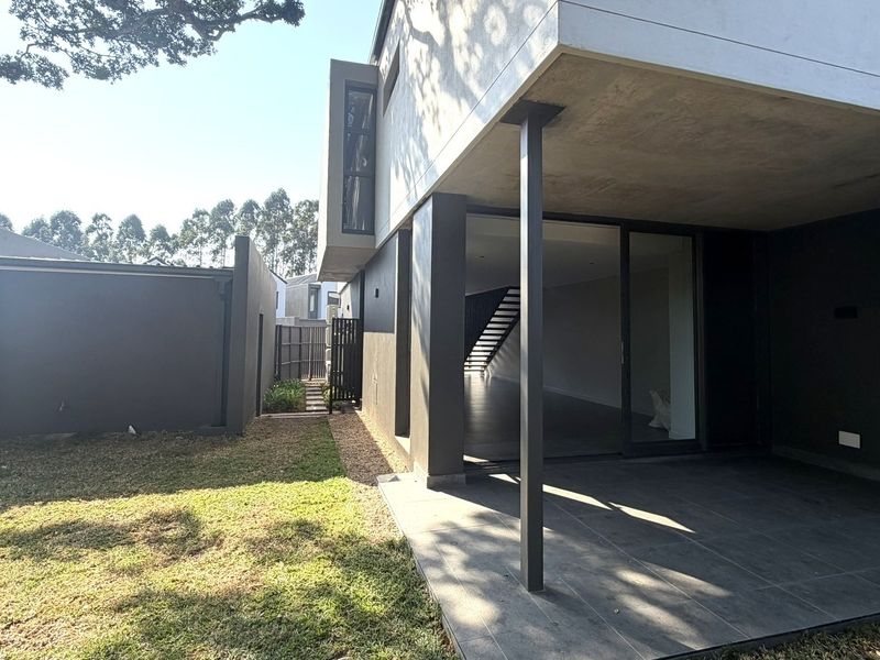 Rear view of the townhouse featuring a covered patio with tiled flooring, sliding glass doors, and access to a private garden area.