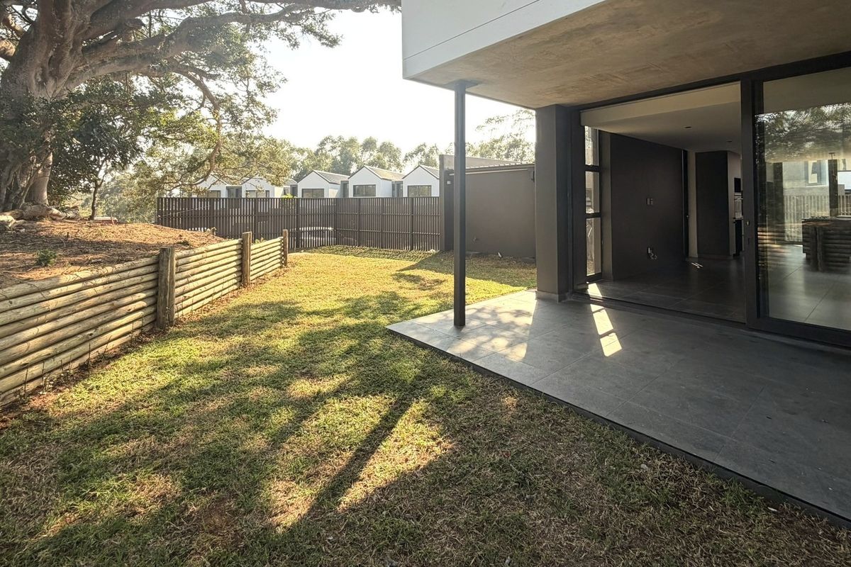 A private rear garden featuring a tiled patio area, timber retaining wall, and mature trees, providing a seamless transition from the indoor living space.