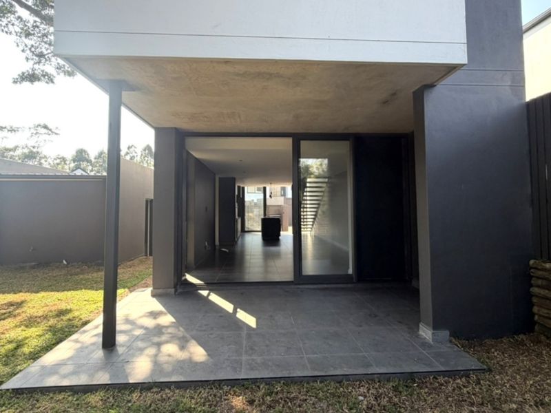 A modern covered patio area with tiled flooring, providing seamless indoor-outdoor flow through large sliding glass doors into the open-plan living space.