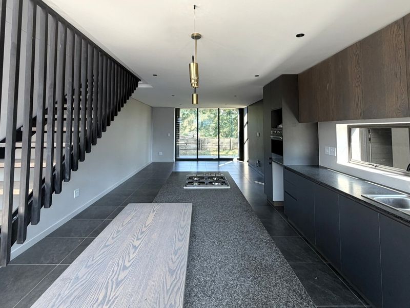 Modern open-plan kitchen and living area featuring sleek dark cabinetry, a central island with a gas hob, and a striking contemporary staircase.