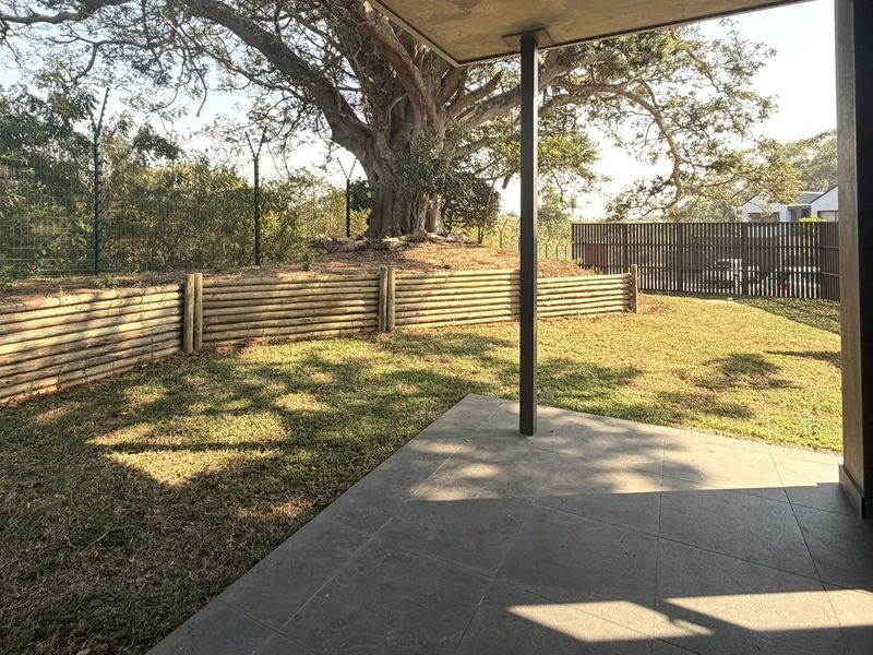 A covered patio area overlooking a private garden with a timber retaining wall and mature tree.