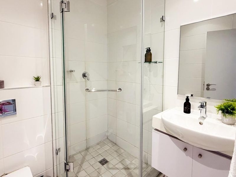 Modern bathroom featuring a glass-enclosed shower, wall-mounted toilet flush system, and a sleek vanity basin with storage cabinet.