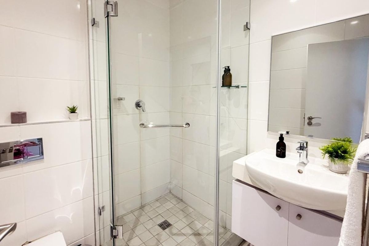 Modern bathroom featuring a glass-enclosed shower, wall-mounted toilet flush system, and a sleek vanity basin with storage cabinet.