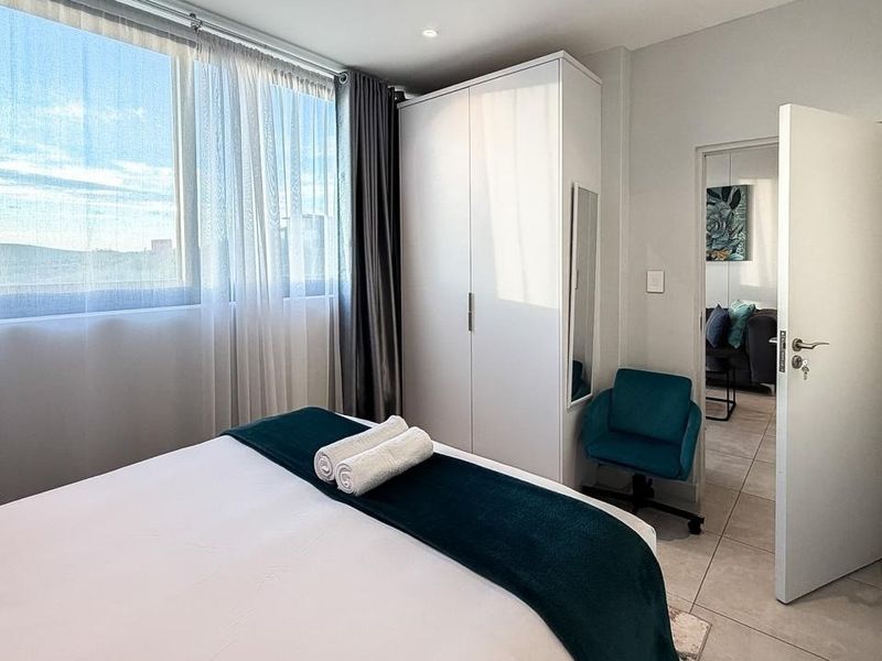 A bright and modern bedroom featuring tiled flooring, a built-in wardrobe, and large windows that provide ample natural light.