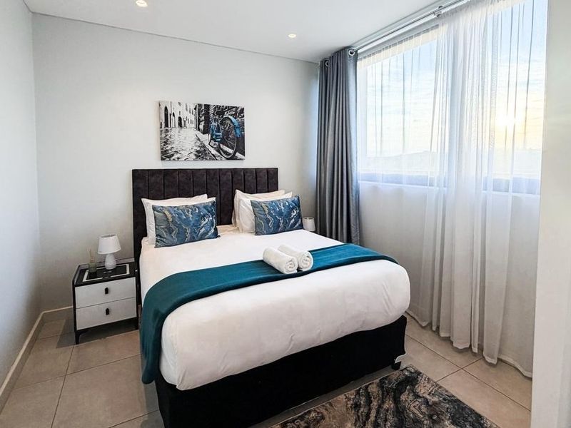 A well-maintained bedroom featuring neutral tiled flooring, recessed ceiling lighting, and a large window allowing for ample natural light.