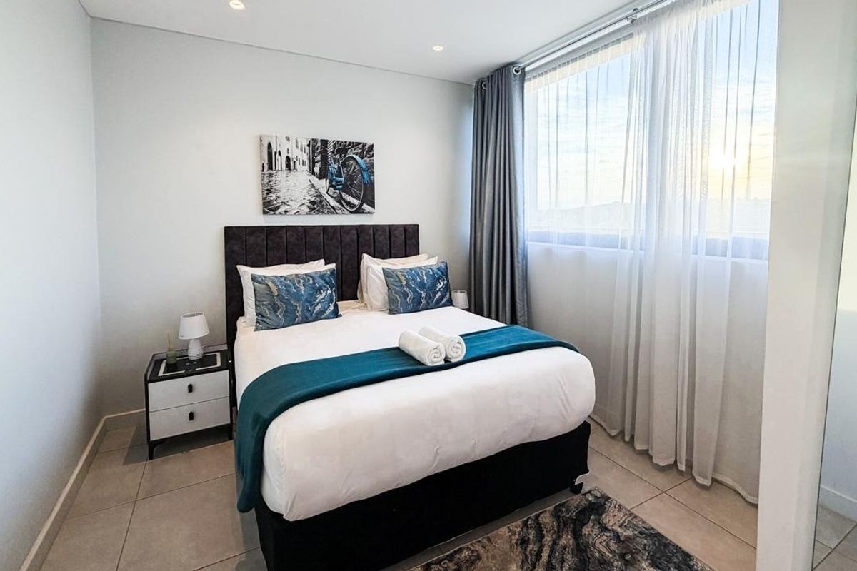 A well-maintained bedroom featuring neutral tiled flooring, recessed ceiling lighting, and a large window allowing for ample natural light.
