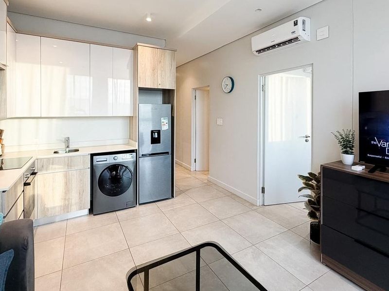 Modern open-plan living area featuring a sleek kitchen with built-in cabinetry, integrated appliances, and tiled flooring, complemented by an air conditioning unit.
