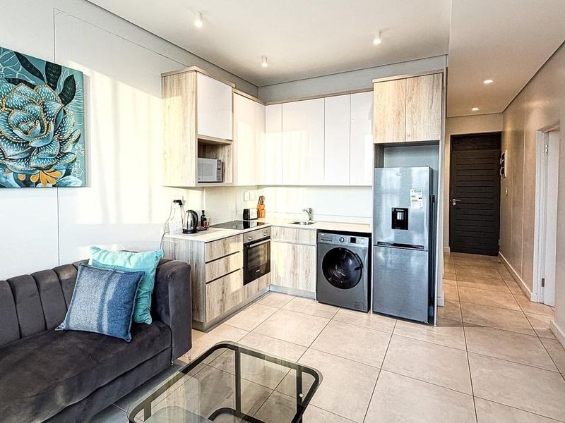 Modern open-plan living area featuring a contemporary kitchen with sleek cabinetry, integrated appliances, and neutral tiled flooring throughout.