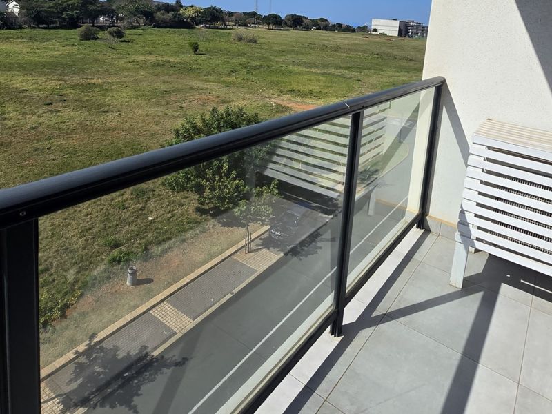 A clean, modern balcony featuring a glass balustrade and tiled flooring, offering an open view of the surrounding landscape.