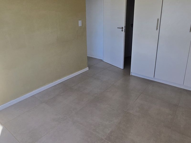 A clean, empty bedroom featuring neutral tiled flooring and built-in white cupboards, offering a blank canvas for personalization.