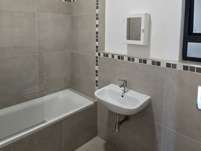 A modern, clean bathroom featuring a bathtub with a glass screen, wall-mounted basin, and neutral tiling throughout.