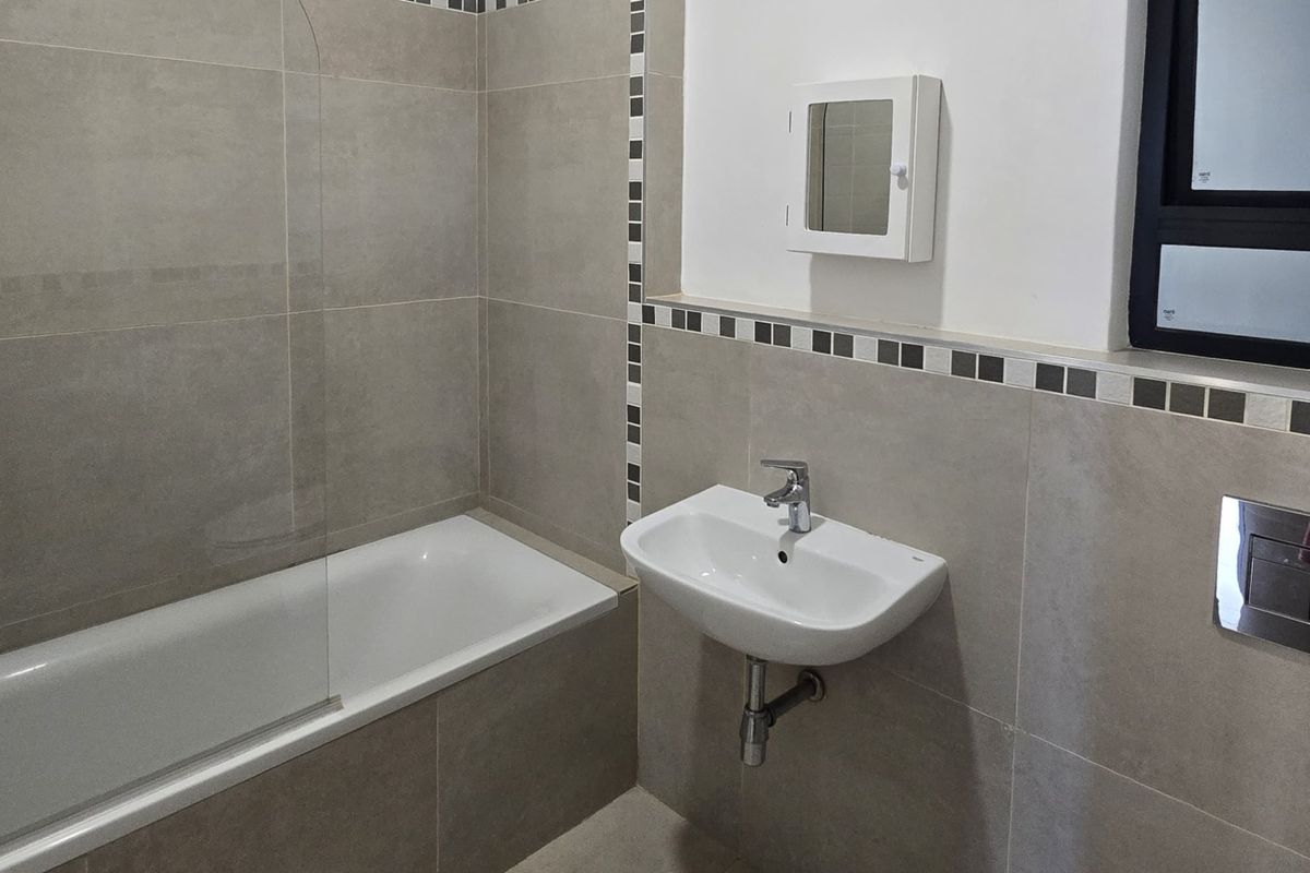 A modern, clean bathroom featuring a bathtub with a glass screen, wall-mounted basin, and neutral tiling throughout.