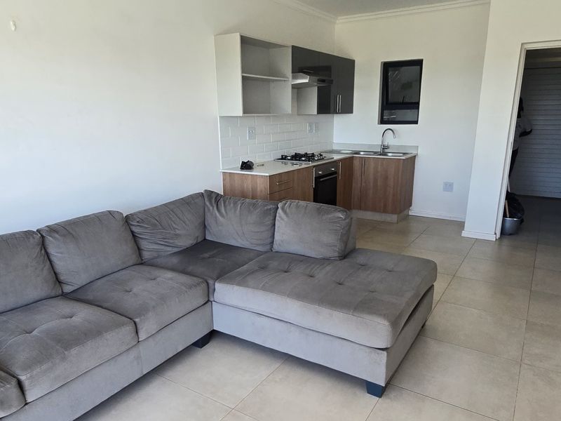 Open-plan living area featuring a modern kitchen with built-in cabinetry, gas hob, oven, and tiled flooring throughout.