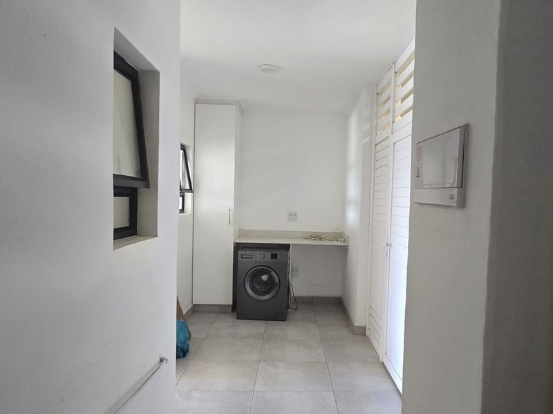 A functional laundry area featuring tiled flooring, built-in cabinetry, a stone countertop, and a louvered door for ventilation.