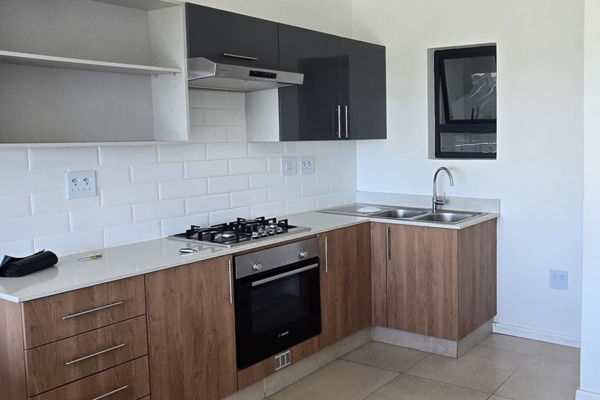 Modern kitchen featuring wood-finish cabinetry, quartz countertops, subway tile backsplash, gas hob, built-in oven, and a double sink with a window view.