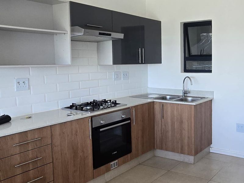 Modern kitchen featuring wood-finish cabinetry, quartz countertops, subway tile backsplash, gas hob, built-in oven, and a double sink with a window view.