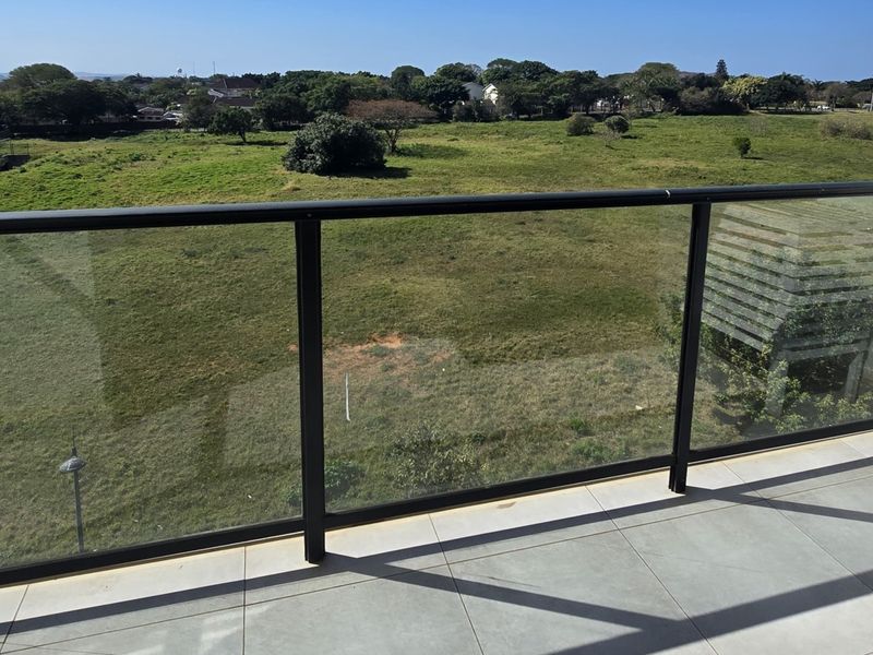 A modern balcony featuring a sleek glass balustrade and tiled flooring, offering an open view of the surrounding landscape.