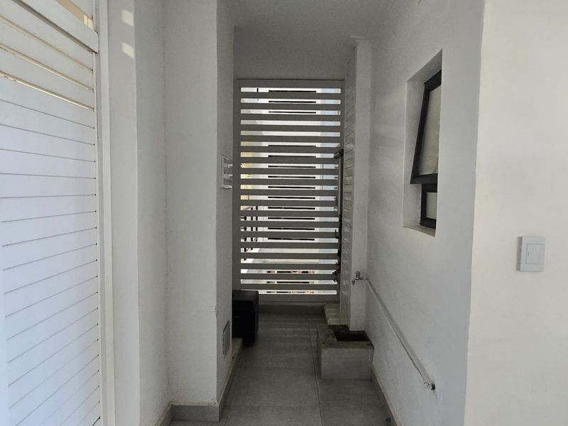 A functional utility space featuring tiled flooring, a slatted privacy screen, and an external water tap, providing a clean and practical service area.