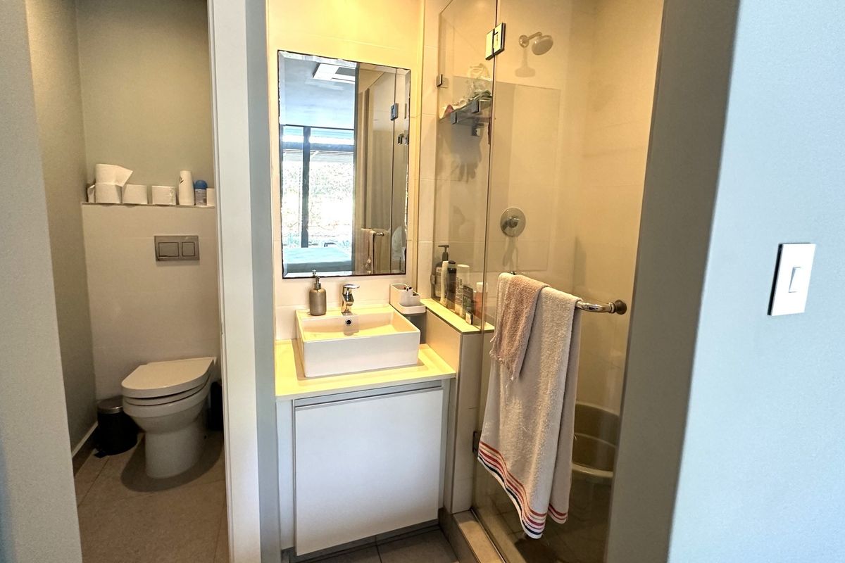 A modern bathroom featuring a wall-hung toilet, a vessel sink with vanity storage, and a glass-enclosed shower area.
