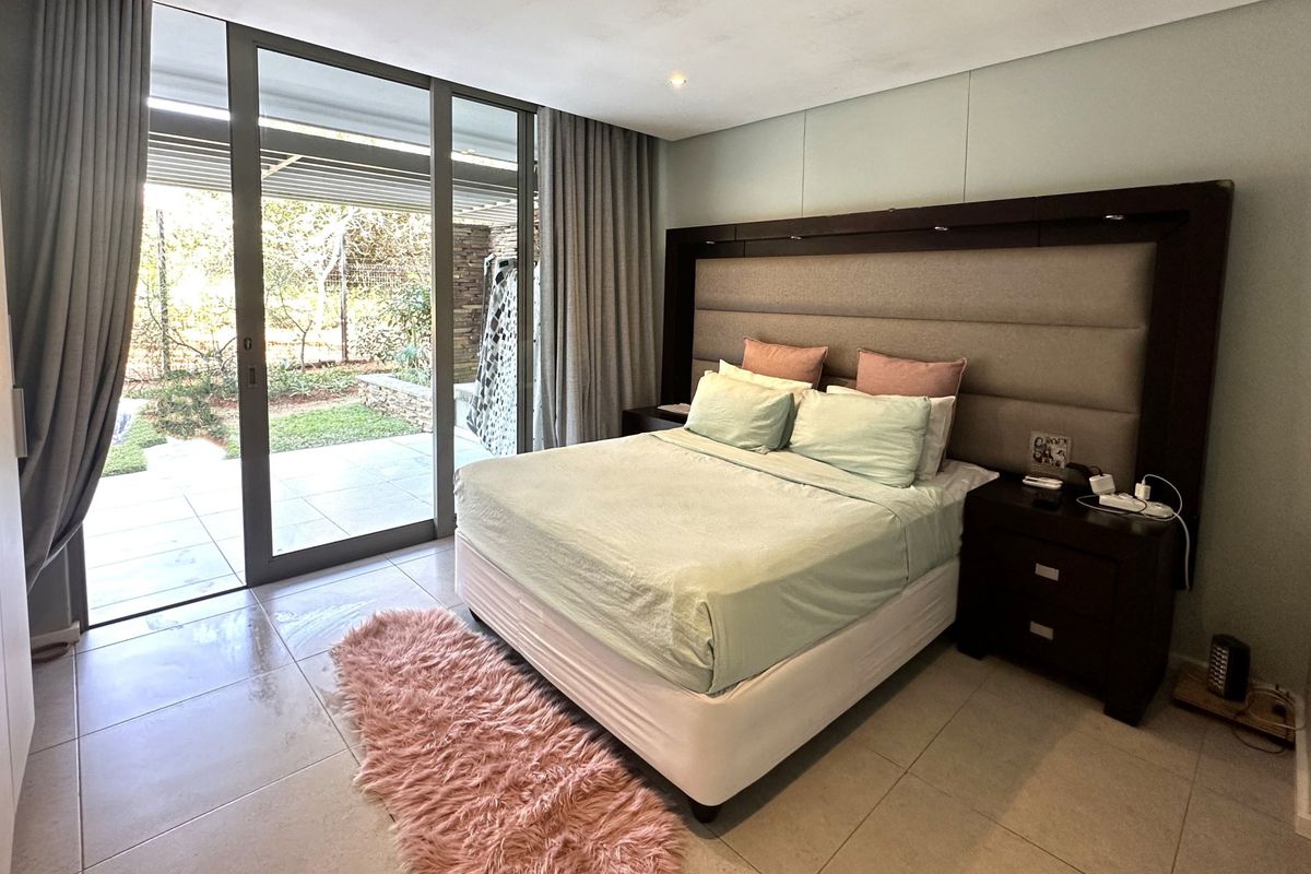 Spacious bedroom featuring large sliding glass doors that open onto a private patio, tiled flooring, and a modern built-in headboard.