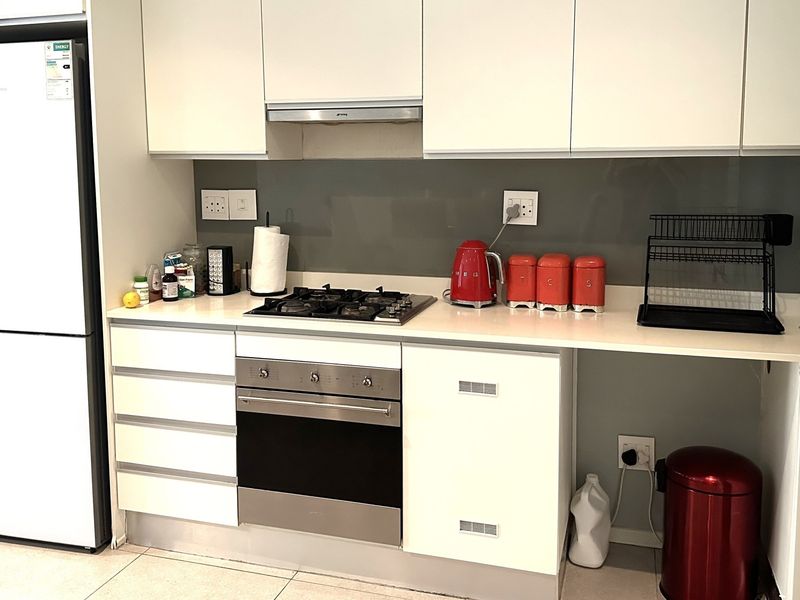 Modern kitchen featuring white cabinetry, stone countertops, a glass splashback, and integrated stainless steel appliances including a gas hob and oven.