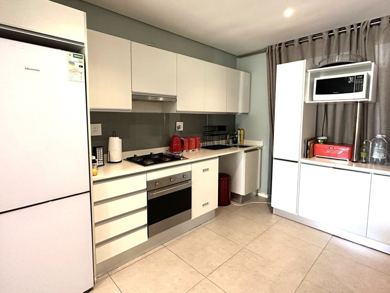 Modern kitchen featuring white cabinetry, stone countertops, integrated oven and hob, and tiled flooring in a clean, functional layout.