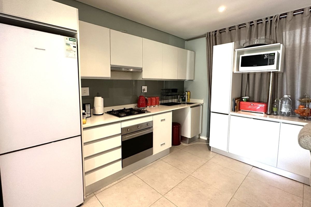 Modern kitchen featuring white cabinetry, stone countertops, integrated oven and hob, and tiled flooring in a clean, functional layout.