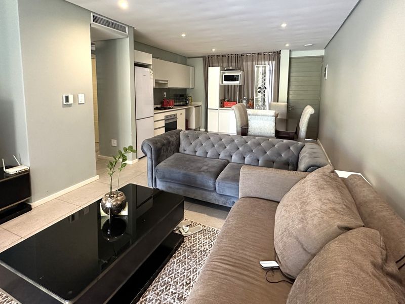Spacious open-plan living and dining area featuring a modern kitchen with built-in cabinetry, integrated appliances, and neutral tiled flooring throughout.