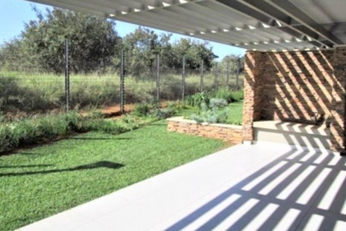 A modern covered patio featuring a stone-clad feature wall with a built-in bench, tiled flooring, and a metal pergola, overlooking a private garden.