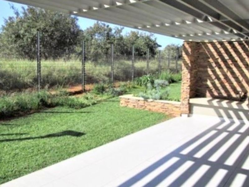 A modern covered patio featuring a stone-clad feature wall with a built-in bench, tiled flooring, and a metal pergola, overlooking a private garden.