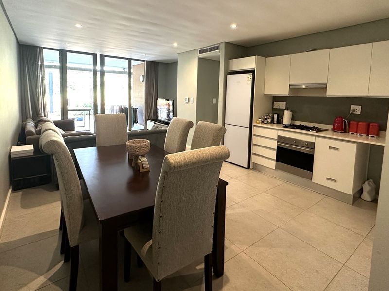 Modern open-plan living area featuring a sleek kitchen with built-in appliances, tiled flooring, and seamless flow to the outdoor patio through sliding glass doors.