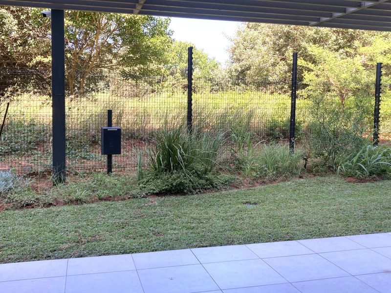 A covered patio area featuring tiled flooring and stone cladding, overlooking a private garden space enclosed by secure perimeter fencing.