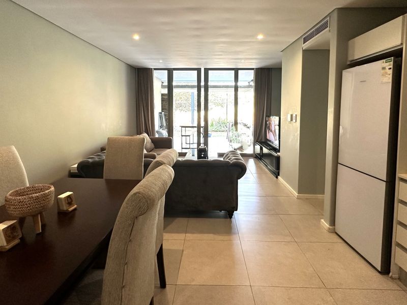 Open-plan living and dining area featuring tiled flooring, recessed lighting, ducted air conditioning, and direct access to an outdoor patio through sliding glass doors.