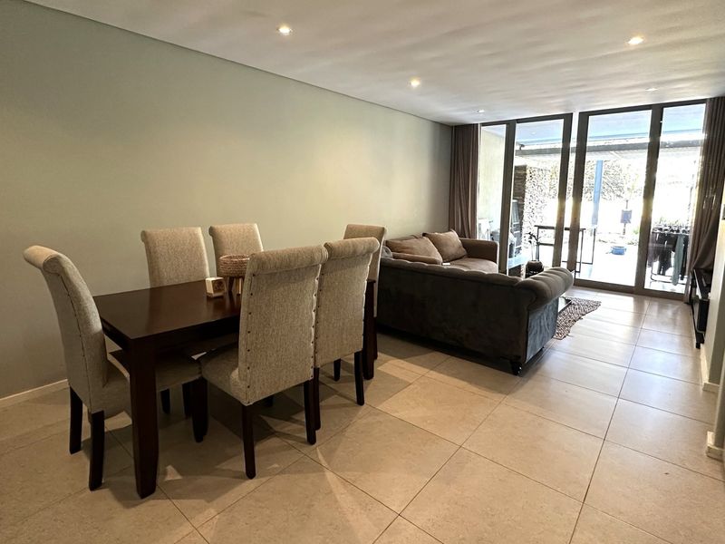 Spacious open-plan living and dining area featuring large format floor tiles, recessed downlighting, and seamless access to the outdoor patio through sliding glass doors.